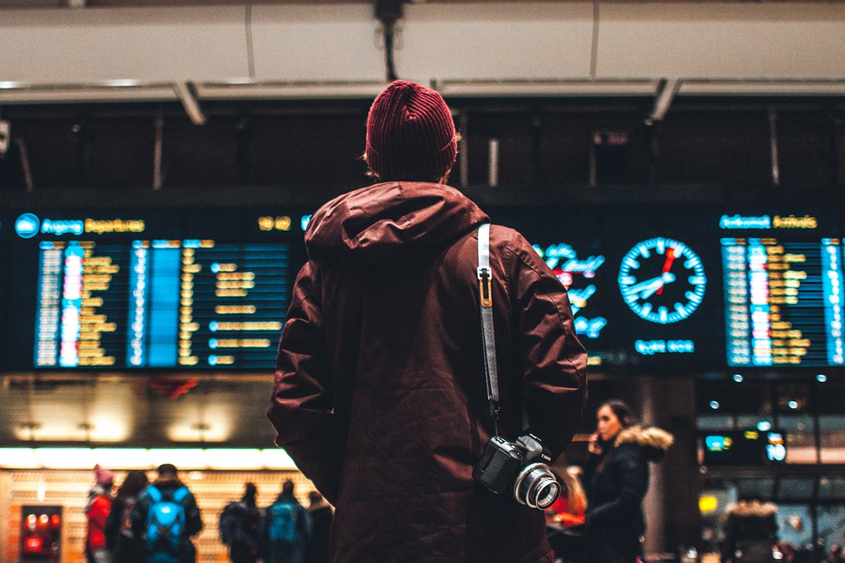 Traveller with a camera slung over his shoulder looking up at an airport departures board