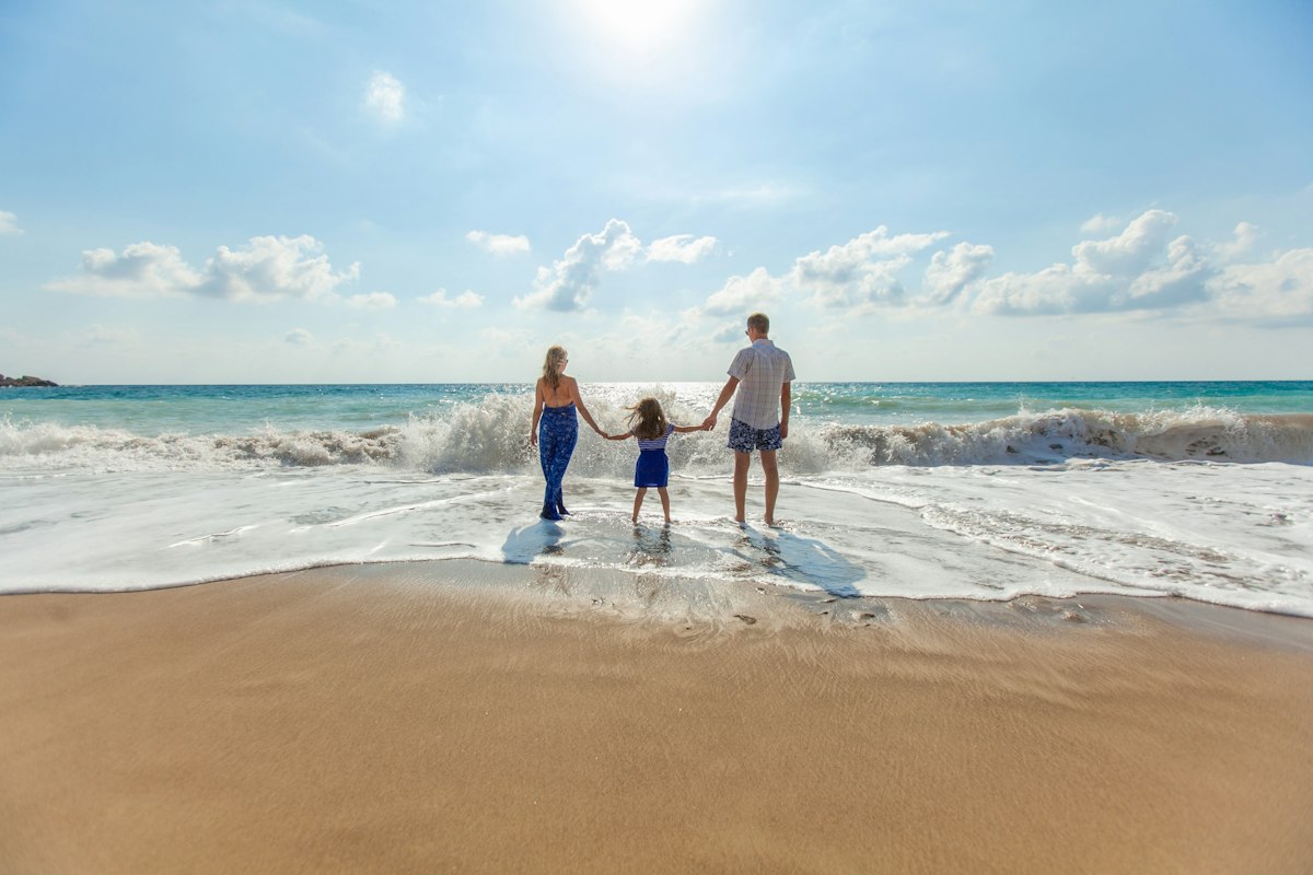 Family holding hands with their young daughter as they walk into the waves on a sunny beach