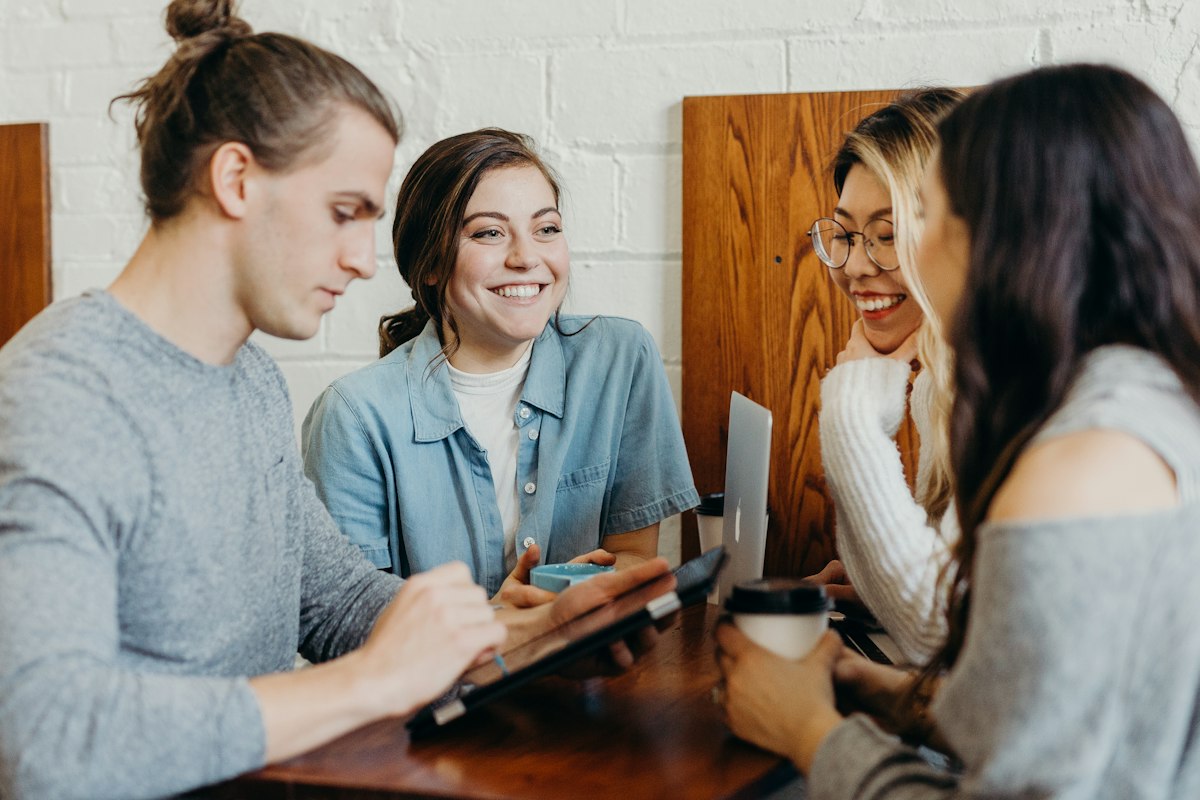 Group of friends round a cafe table smiling and looking at a phone together