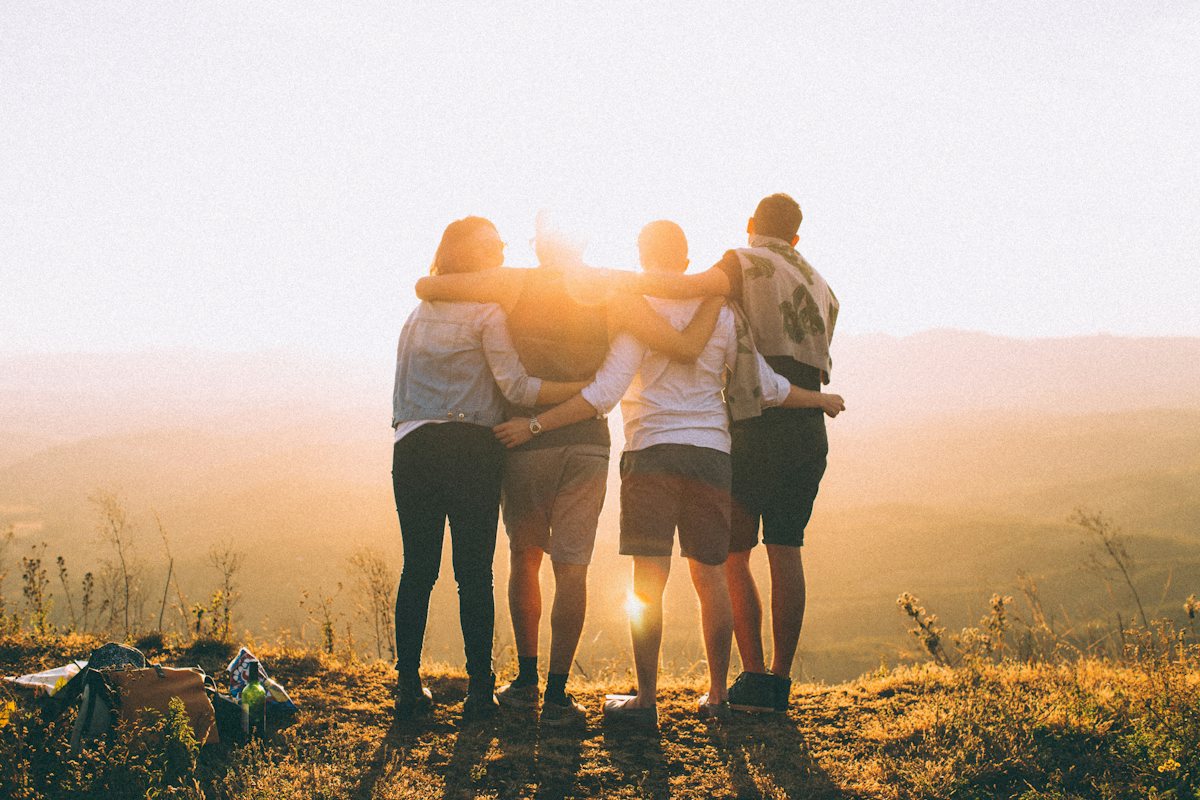 Four friends with their arms round each other watching the sun set over the hills