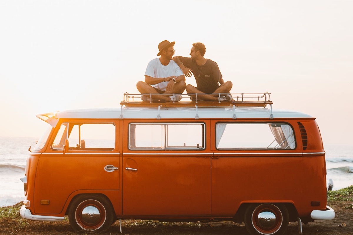 Two friends sitting on the roof of an orange camper van at sunset